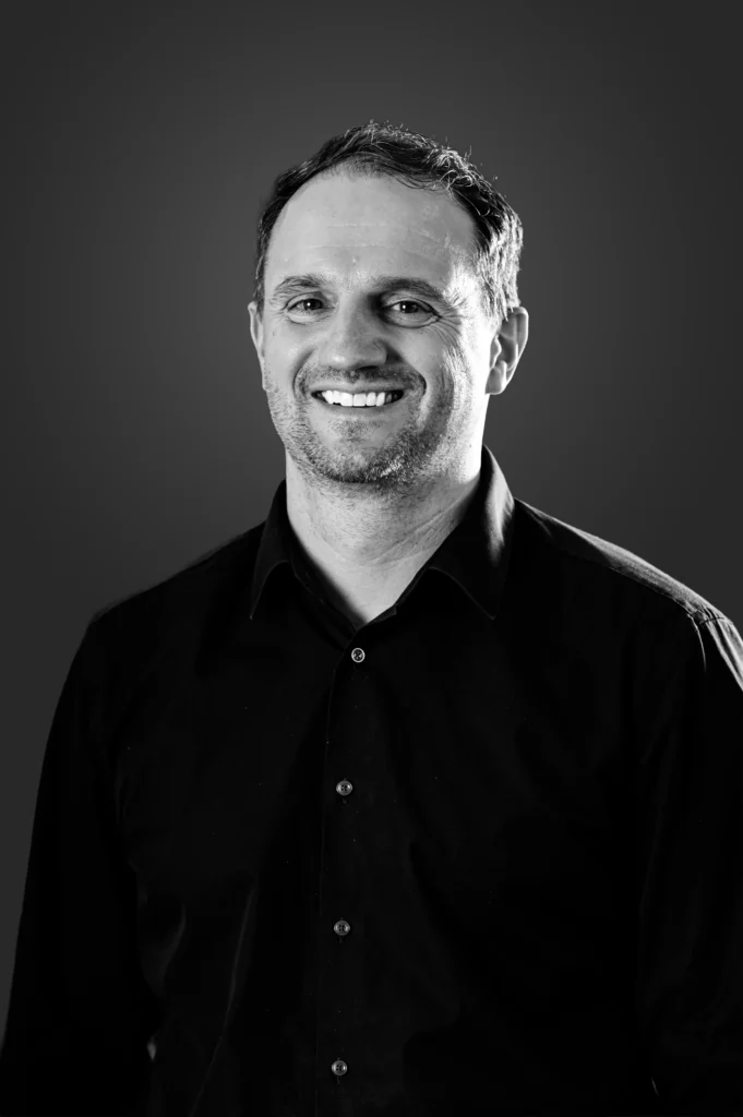 Smiling person in black shirt, grayscale photo.