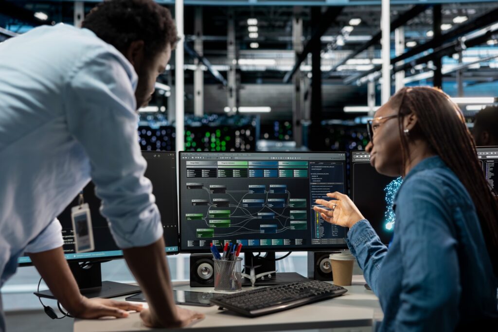 Two people discussing data on computer screens.