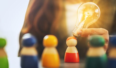 Hand holding light bulb over toy figure.