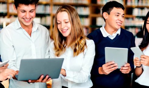 Group of students using digital devices in the Axsos Academy library.